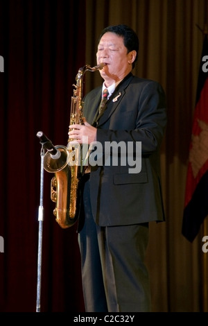 Une mobilité aveugles (sans vision) Asian homme portant un costume et une cravate joue un saxophone à Vientiane, au Laos. Banque D'Images