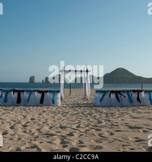 Une plage déserte pour une cérémonie de mariage. Les housses de chaises sont blanches avec des arcs bleu et brun. Une arche attend le couple. Banque D'Images