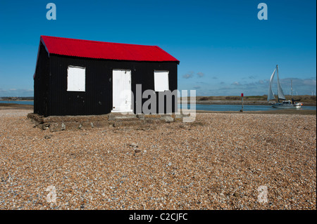 Yacht blanc voiles passé Norton cabane sur la plage de galets Rye East Sussex avec un parc éolien à la distance Banque D'Images