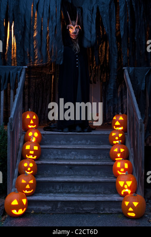 Les citrouilles sculptées allumé effrayant au crépuscule dans les escaliers avec le démon avec des cornes sur le porche maison hantée pour Halloween Banque D'Images