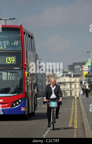 Un homme sur un vélo cycliste Boris Bike à Londres, en Angleterre avec un bus passant Banque D'Images