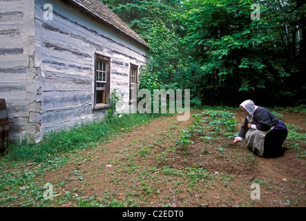1, une femme canadienne, le désherbage, jardin, portant des costumes d'époque, le Village Historique Acadien, près de ville de Caraquet, Nouveau-Brunswick, Canada Province Banque D'Images