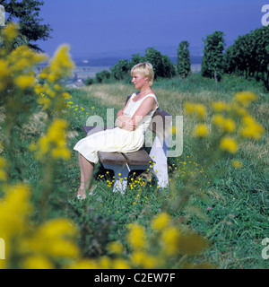 Menschen, Freizeit, Urlaub, Erholung, junge Frau im Sommerkleid sitzt auf einer sich und entspannt Holzbank Banque D'Images