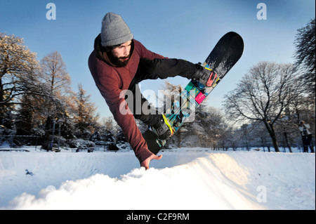 Un homme monte un snowboard sur un skatepark couvert de neige dans le parc de Kelvingrove, Glasgow, Ecosse. Banque D'Images