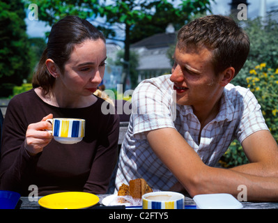 L'homme et la femme parle de boire du thé et manger des gâteaux dans le café en plein air Banque D'Images