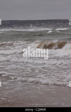 La ville de North Rustico Harbour comme vu au-delà de vagues déferlant sur la côte nord de l'Île du Prince Édouard, Canada Banque D'Images