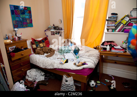 Une adolescente en désordre university la chambre de l'élève dans son appartement, UK - ordinateur portable sur le lit, des vêtements et des livres partout Banque D'Images