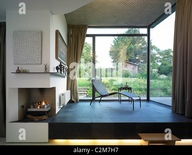 Extension maison moderne en bois avec coin salon, rideaux de fenêtre, coin photo coin cheminée allumé et vue sur le jardin Banque D'Images