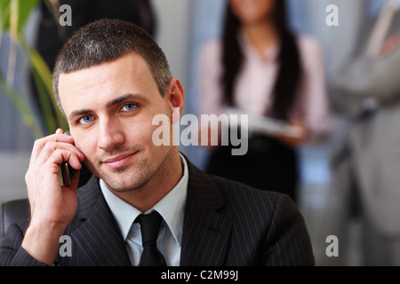 Bel homme d'exécutif au téléphone pendant que son équipe travaille derrière Banque D'Images