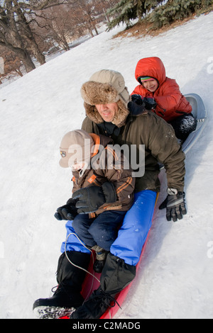 Garçon et fille de 6 et 7 en glissant sur l'hiver neigeux Merriam Park Hill avec papa l'âge de 42 ans. St Paul Minnesota MN USA Banque D'Images