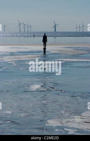 L'un des 100 hommes de fer à Crosby Beach dans le cadre d'Anthony Gormley a un autre endroit, avec des générateurs du vent derrière, Liverpool, Banque D'Images