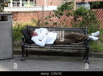 Un homme endormi sur un banc dans une ville du Royaume-Uni. Banque D'Images