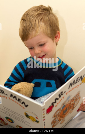 Jeune garçon lisant un livre, sur son lit. Banque D'Images