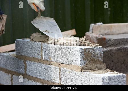 Maçon la construction d'un mur en parpaings de ciment avec la moitié de la construction d'un mur de soutènement en bloc dans le flou d'une truelle en france Banque D'Images