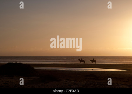 Deux cavaliers sur la plage au coucher du soleil Banque D'Images