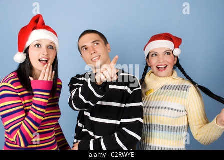 Groupe de jeunes amis wearing Santa hats et montrant le bonheur et surpris visages tandis que l'homme pointing Banque D'Images