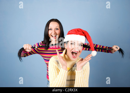 Un Funny Girl with Santa hat d'avoir ses tresses tiré par son amie et les deux rient et de crier et de s'amuser Banque D'Images