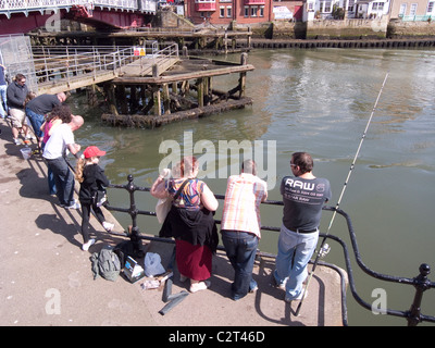 Les vacanciers dans soleil du printemps par le pont de pêche dans le port de Whitby Banque D'Images