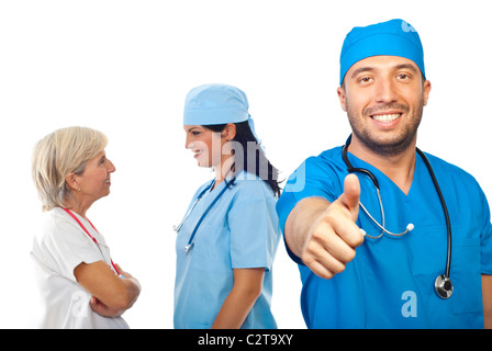 Doctor giving thumb up mâle en face de droit alors que son équipe d'avoir la conversation et rire en arrière-plan Banque D'Images
