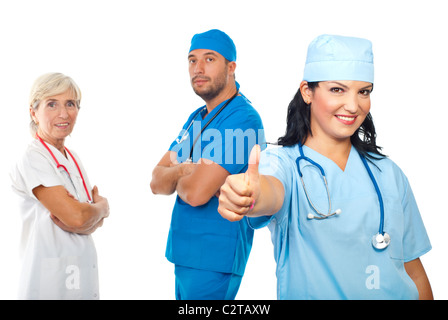 Groupe réussi de trois médecins debout avec les mains croisées et une jeune femme médecin giving thumb up in front of camera Banque D'Images