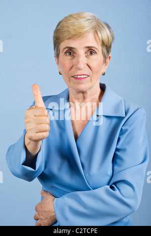 Blonde senior business woman giving Thumbs up and smiling on blue background Banque D'Images