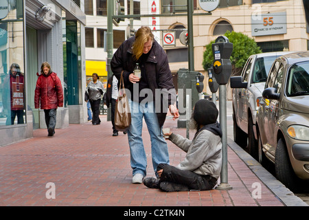 Une femme donne l'argent à un sans-abri panhandler juste à côté de Market Street à San Francisco. Banque D'Images