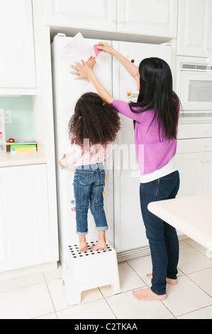 Mother putting daughter's dessin sur réfrigérateur Banque D'Images