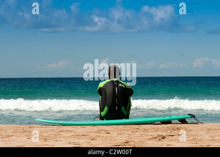 Surfer assis sur la plage en attendant le surf, El Cotillo, Fuerteventura, Îles Canaries Banque D'Images