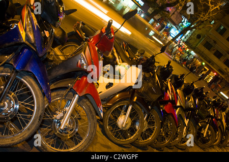 Vue horizontale d'une ligne de cyclomoteurs et scooters garés sur le trottoir dans une rangée à Hanoi la nuit. Banque D'Images