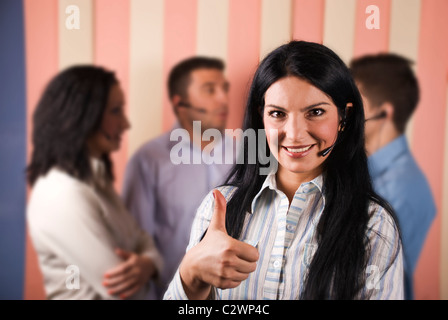 Happy customer service rep smiling et giving Thumbs up en face de l'image avec son équipe debout en arrière-plan Banque D'Images