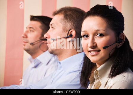 Personnes avec casque de travail dans un centre d'appels,jeune femme confrontés et vous sourit et hommes debout de profil Banque D'Images