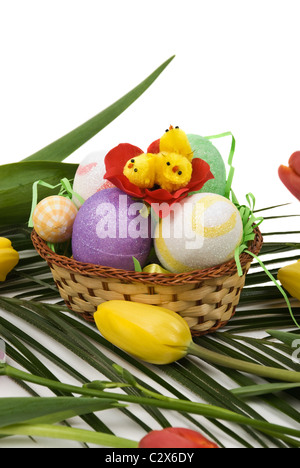 Décoration de Pâques avec des œufs et du poulet dans un panier et tulipes rouge et jaune sur une feuille d'un palmier Banque D'Images