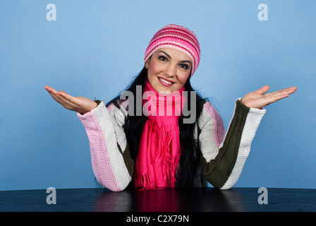 Hiver femme assis à table avec l'expression du visage de sourire et de poser et tenir la main tendue sur fond bleu Banque D'Images