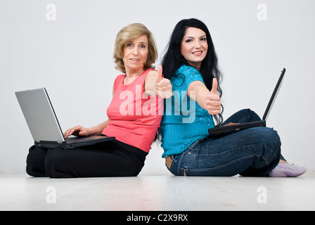 Deux femmes ,smiling mother and daughter sitting on white parquet dans la chambre,stand dos à dos chaque ordinateur portable utilise un Banque D'Images