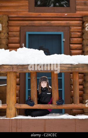 Caucasian girl sitting on snowy porch Banque D'Images