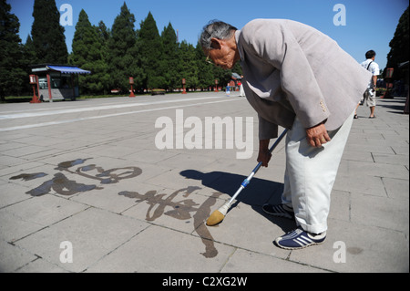 Un vieil homme chinois Calligraphie écriture sur le sol avec un gros pinceau et de l'eau Banque D'Images