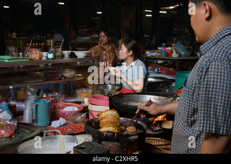 Une femme est en train de manger et d'un homme est la cuisson des aliments à l'intérieur du Cambodge le marché russe à Phnom Penh, Cambodge. Banque D'Images