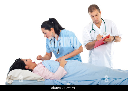Femme médecin examiner pour mal de gorge patient dans un lit d'hôpital tandis que d'autres médecin écrit dans le presse-papiers Banque D'Images