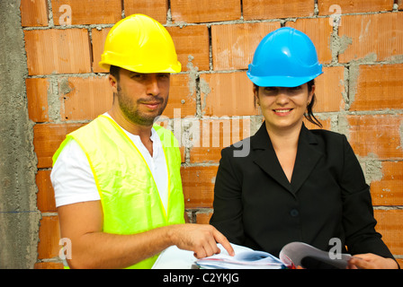 Deux jeunes architectes souriant avec des plans du site et les plans d'exploitation,homme pointant au papier Banque D'Images