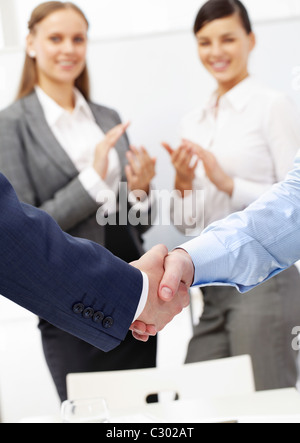 Photo de handshake de partenaires d'affaires après avoir heurté un accord sur fond de deux femmes applaudir Banque D'Images