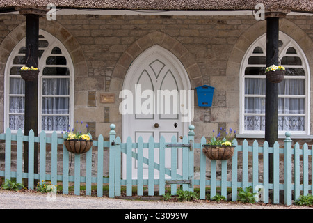 Quaint cottage traditionnel avec un toit de chaume, porte de style gothique, paniers suspendus, paling clôture, Cornwall, England, UK Banque D'Images