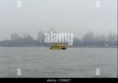 En un jour brumeux au printemps, un New York Water Taxi traverse le port de New York, à Brooklyn dans l'arrière-plan. Banque D'Images