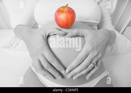 Smiling pregnant woman in high key mono avec une pomme rouge sur son ventre Banque D'Images