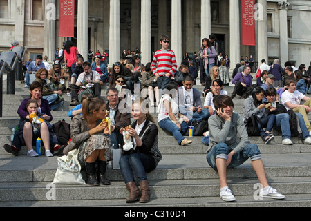 Des groupes de gens assis sur les marches à Trafalgar Square, Londres, Angleterre avec la National Gallery de l'arrière-plan Banque D'Images