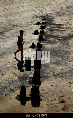 Les jeunes en silhouette près de brise-lames sur le sable à marée basse. Banque D'Images