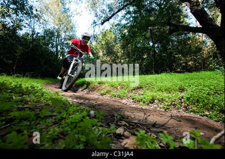 Un jeune homme chevauche son vtt de descente sur un chemin entouré de verdure très trèfles. Banque D'Images