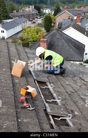 L'homme travaillant sur toit de maison dans village equerres de fixation pour installation photovoltaïque solaire Wales UK Banque D'Images
