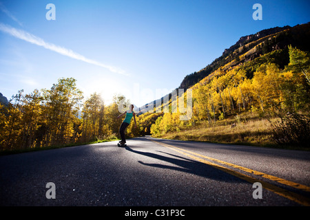 Une jeune femme dans un pays lisse longboards route à travers les montagnes et les forêts d'or. Banque D'Images