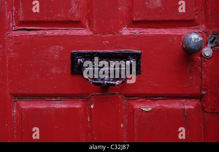 Détail de scarlet red porte avant avec petit mobilier noir letterbox combinés et knocker plus poignée dans le besoin de peinture Banque D'Images