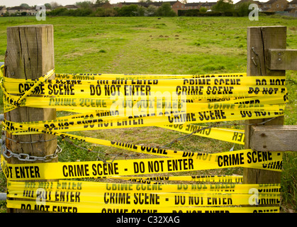 Scène de crime - bande jaune n'entrez pas - entre les poteaux de bois avec terrain en arrière-plan. Banque D'Images